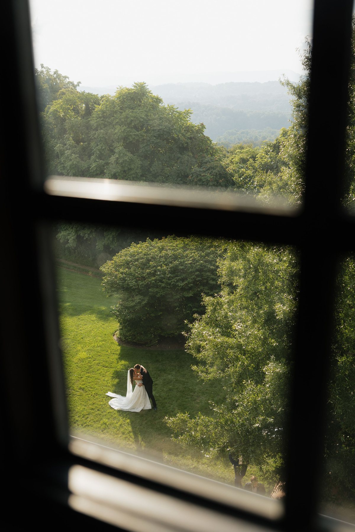 Couple seen through a window frame, embracing on a lawn above a green valley