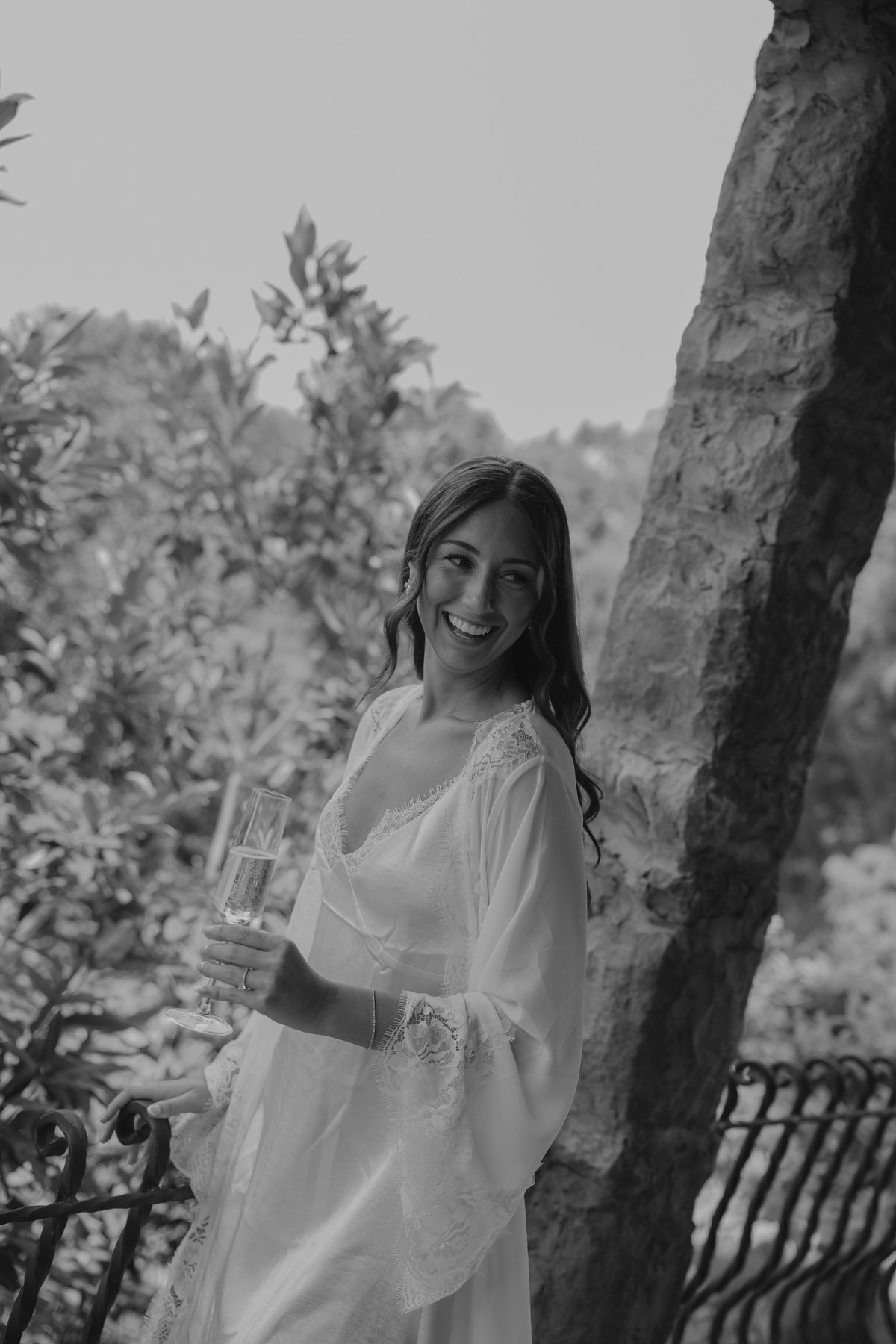 Bride in a lace robe holding a champagne glass, black and white