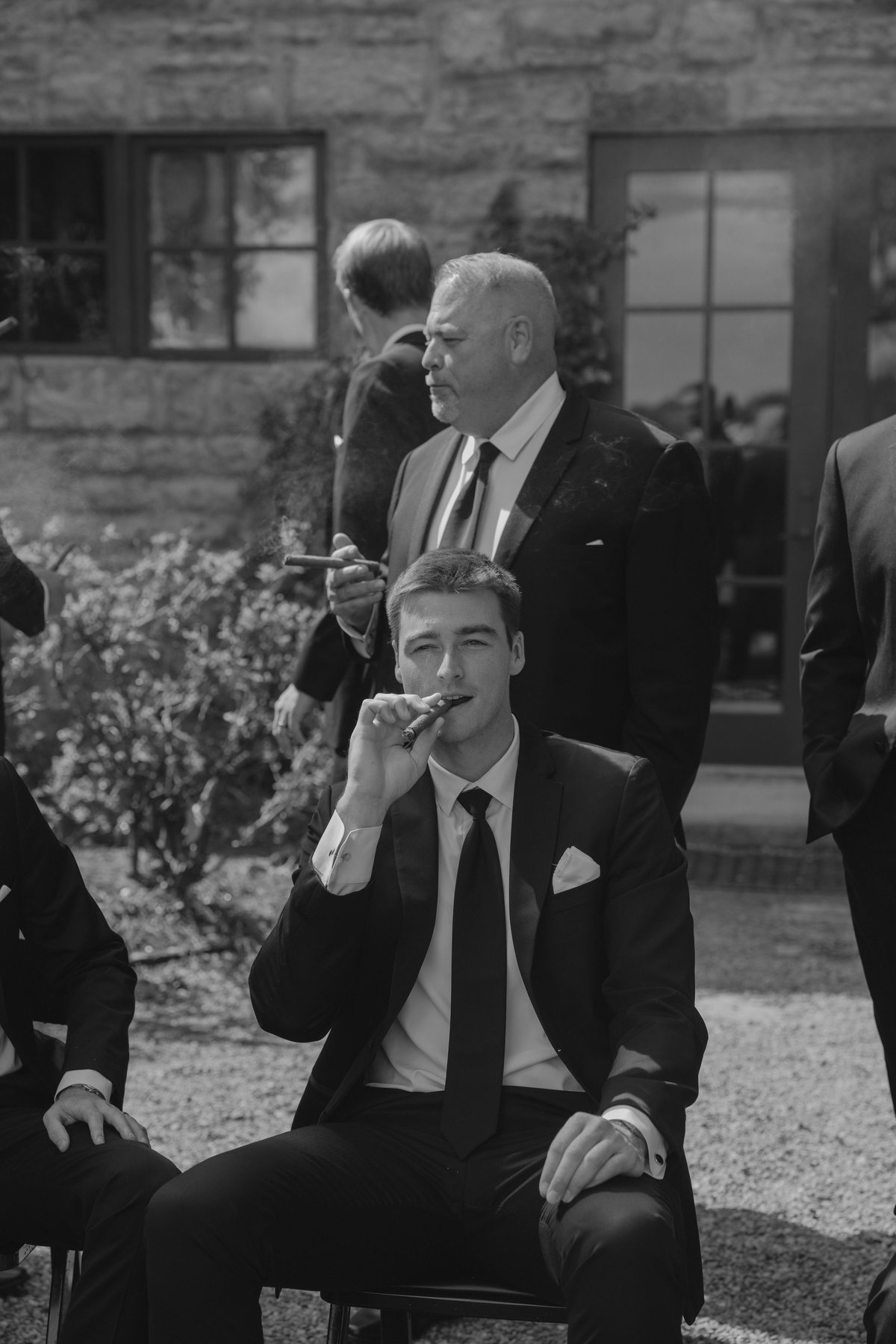 Groom and groomsmen with cigars outside a stone building, black and white