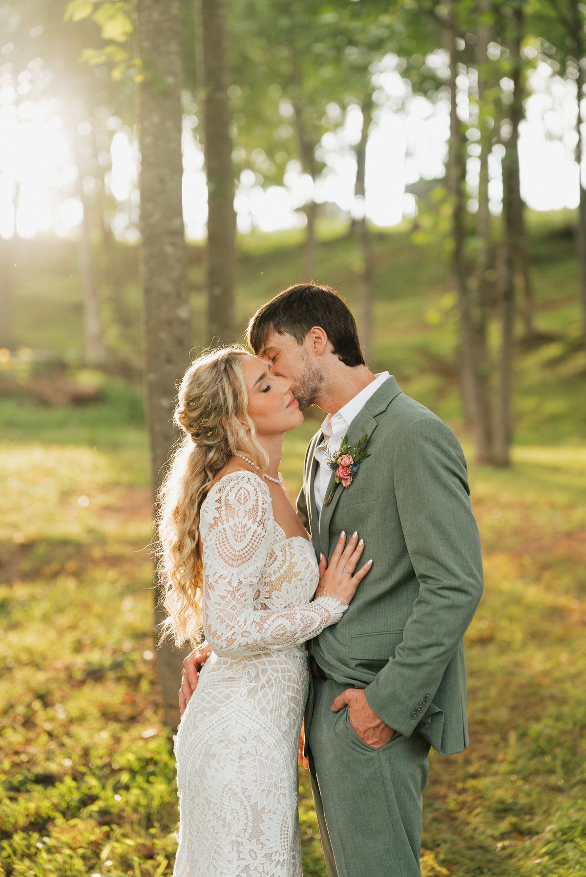 Couple in a sunlit forest, groom in a sage green suit