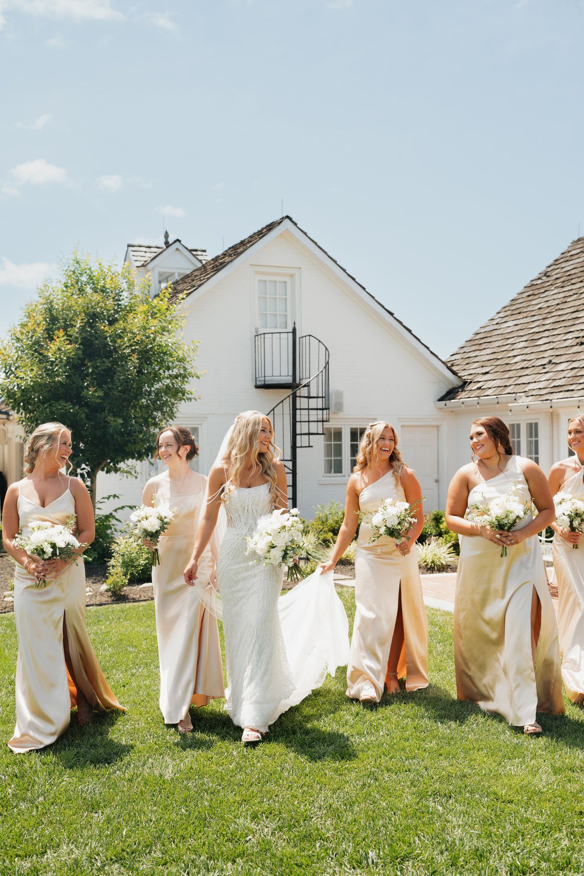 Bride walking with her bridesmaids in cream dresses outside a white barn