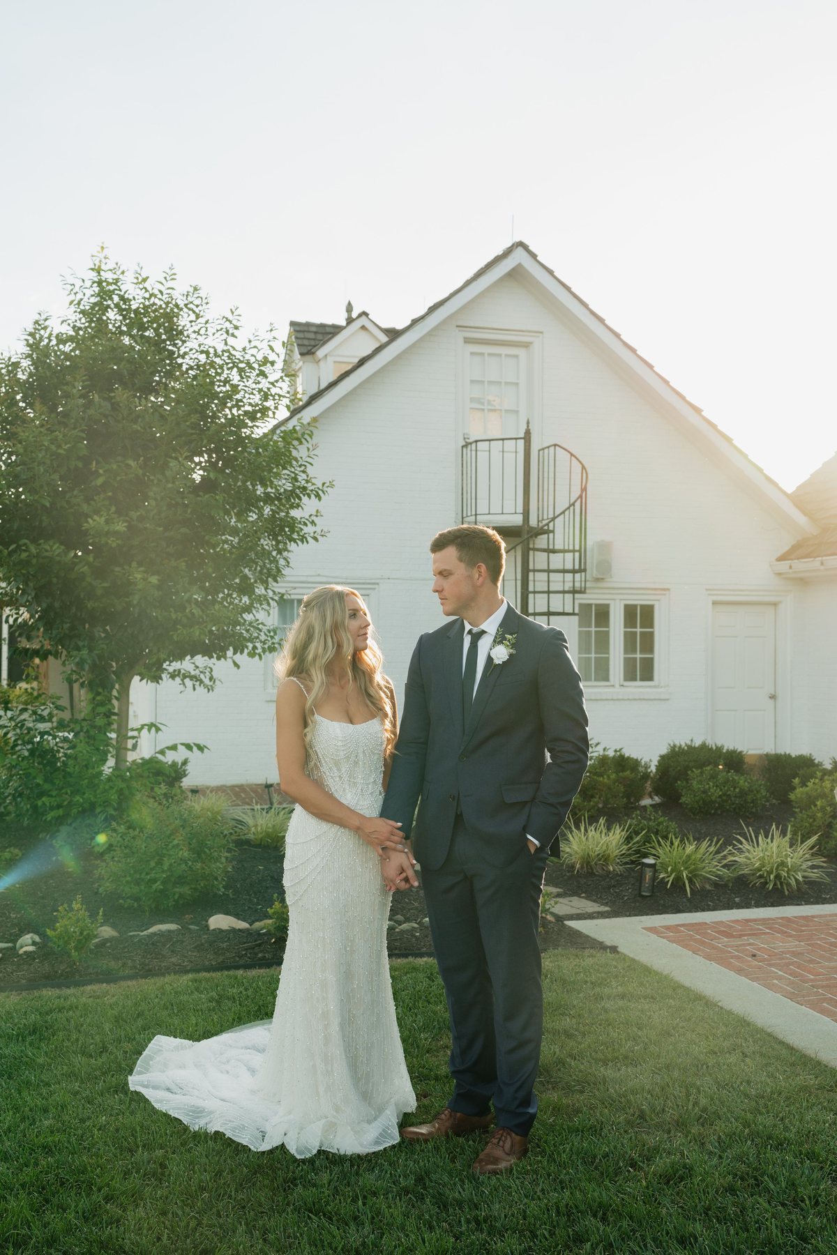Couple holding hands at golden hour in front of a white farmhouse