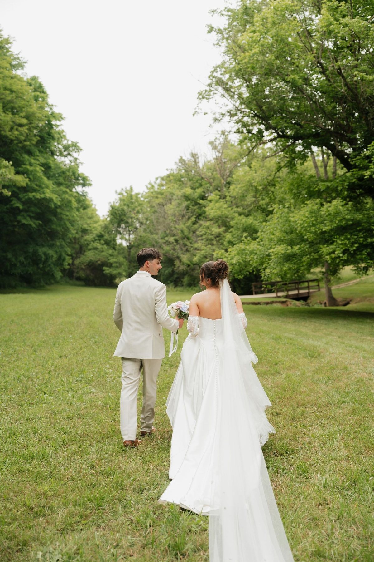 Couple walking through a green field toward a footbridge