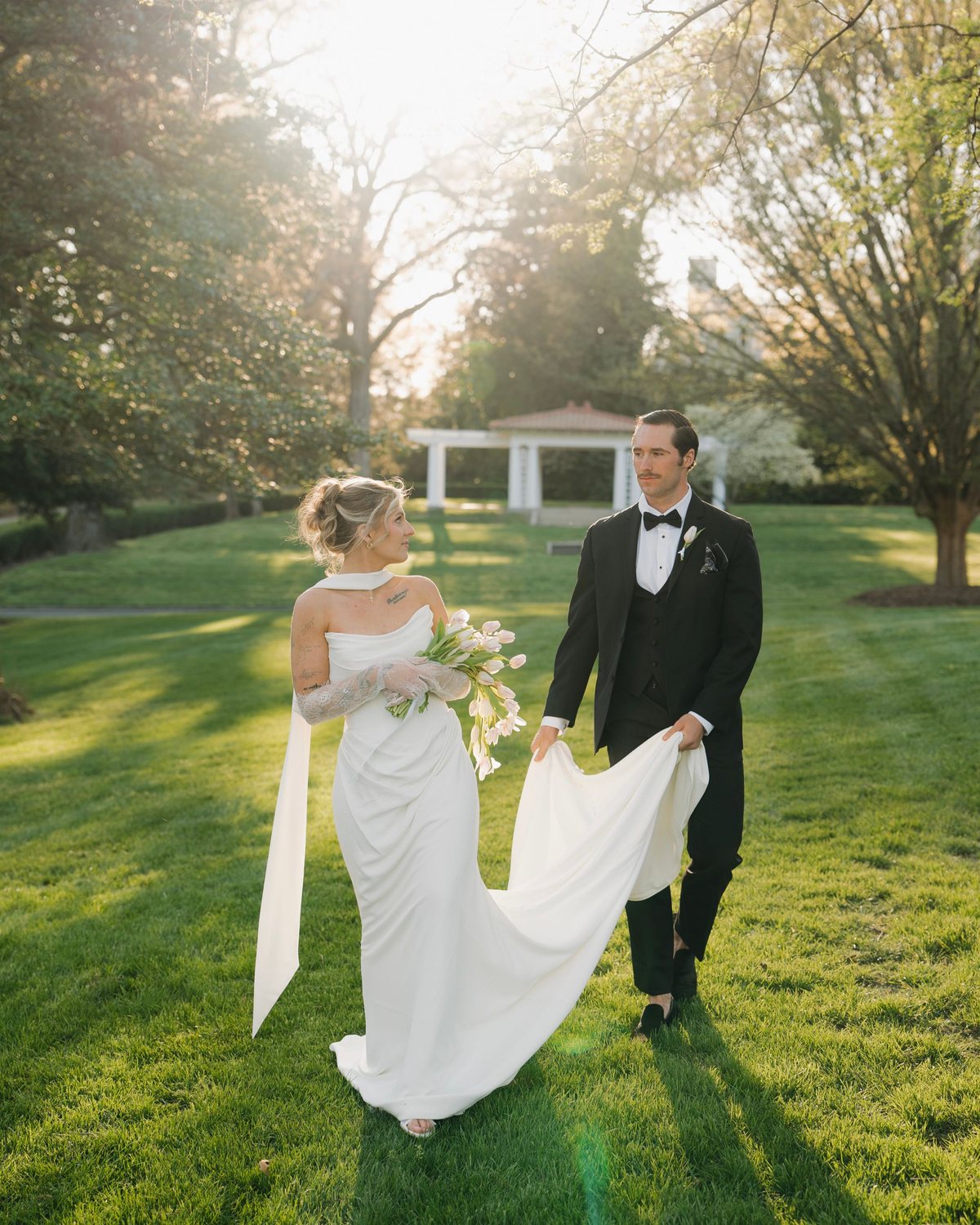 Bride with tulips looking back at her groom who carries her train